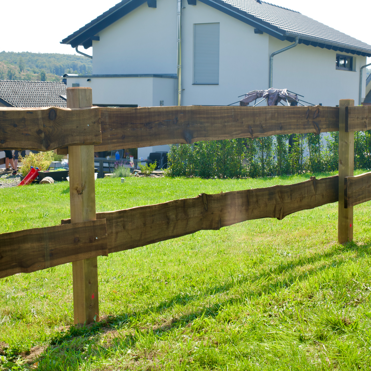 Holz Weidezaun mit Vierkantpfosten als Grundstücksgrenze auf Rasen vor einem Wohnhaus