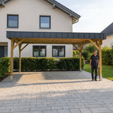 Mann steht neben dem Holzdoppelcarport Amecke Premium auf der Einfahrt vor dem Haus